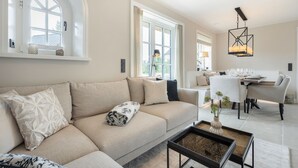 Ein modernes Wohnzimmer mit einem beigen Sofa, einem Couchtisch und einem Essbereich mit Tisch für vier Personen.