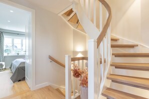 Un escalier moderne avec des marches en bois et des rampes blanches, menant à une pièce comprenant un lit et une fenêtre.