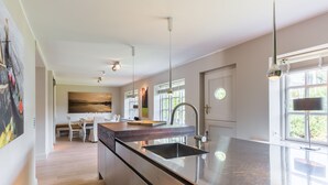 Une cuisine moderne dotée d’un grand îlot central, d’appareils électroménagers en acier inoxydable et de luminaires suspendus.