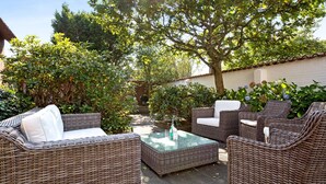 Un espace patio aménagé avec des meubles en osier, notamment des canapés et une table basse, entouré de verdure et d’arbres.