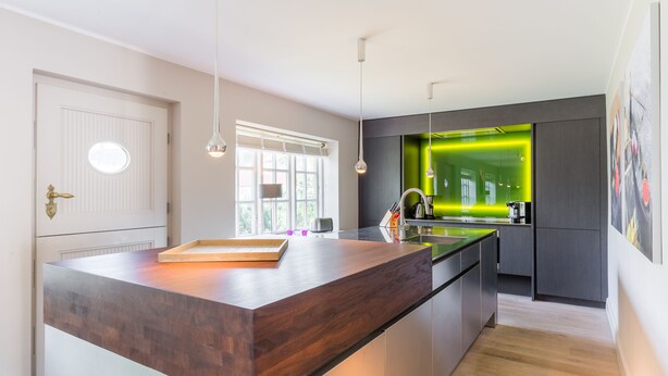 Une cuisine moderne dotée d’un îlot central, de luminaires suspendus et d’un mur d’accent vert.