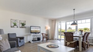 Uma sala de estar moderna com sofá, televisão, mesa de jantar e cadeiras.
