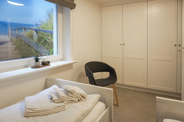 Ein Schlafzimmer mit Bett, Stuhl, Kleiderschrank und Fenster mit Blick auf einen Strand.