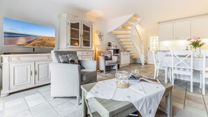 Un vaste espace de vie comprenant un grand téléviseur à écran plat, une table à manger avec des chaises, un escalier et un coin cuisine.