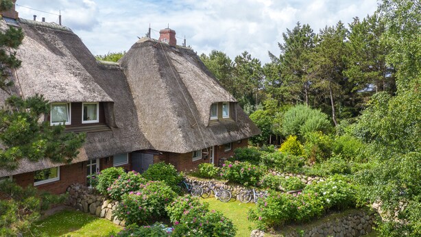 Une maison traditionnelle à toit de chaume, avec un jardin et des vélos.