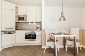 A modern kitchen with white cabinetry, a dining table with wicker chairs, and a hanging light fixture.