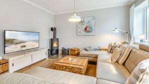 A modern living room with a flat-screen TV, a wooden coffee table, a sofa, a fireplace, and a painting of a sailboat. - Warme Farben, ein Hochwertiger Holzboden und Maritim Blaue Accessoires (List auf Sylt)