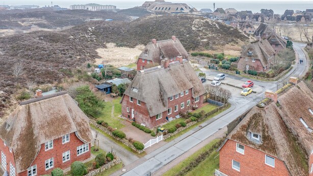A rural village with traditional thatched-roof houses, a main road, and a large fort in the background. - Warme Farben, ein Hochwertiger Holzboden und Maritim Blaue Accessoires (List auf Sylt)