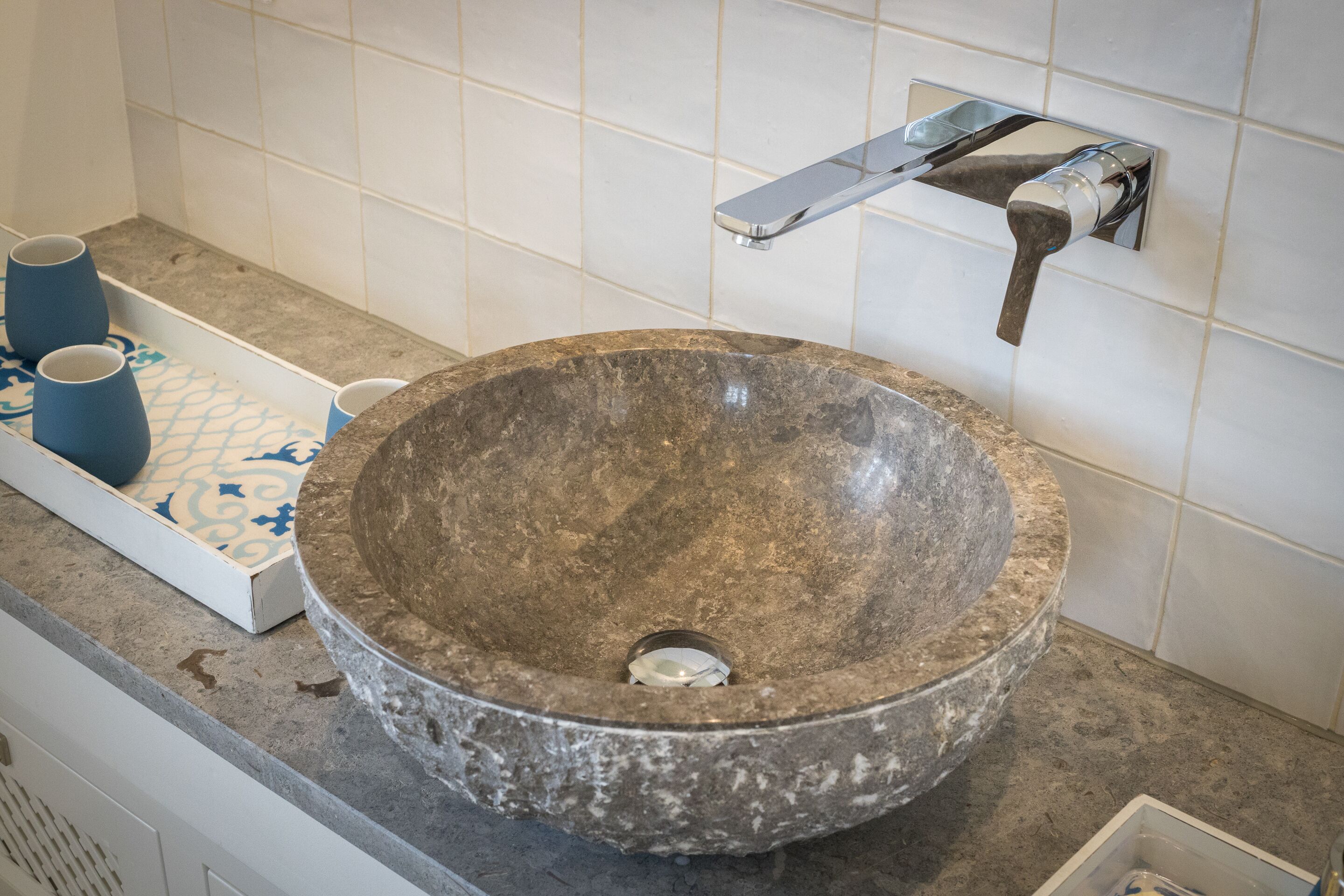 Une salle de bain avec un grand lavabo rond en pierre, un robinet moderne et un petit plateau sur lequel reposent deux tasses bleues.