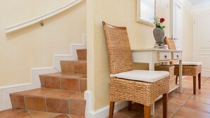 A staircase with beige walls and brown tiles, leading to a landing with a wicker chair and a small table with a vase and a red flower. - Zentral, Aber Dennoch Sehr Ruhig und Strandnah Gelegen (Wenningstedt-Braderup (Sylt))