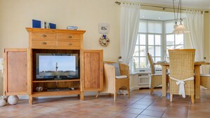 A living room with a wooden entertainment unit, a television, wicker chairs, and a dining table. - Zentral, Aber Dennoch Sehr Ruhig und Strandnah Gelegen (Wenningstedt-Braderup (Sylt))