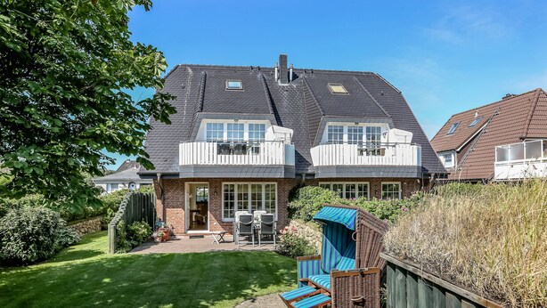 A two-story house with a well-maintained lawn, a patio with outdoor furniture, and a wooden fence. - Zentral, Aber Dennoch Sehr Ruhig und Strandnah Gelegen (Wenningstedt-Braderup (Sylt))