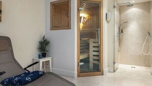 Une salle de bain moderne avec une douche à parois de verre, une porte en bois et une petite table blanche sur laquelle est posée une plante en pot.