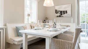 Un coin repas avec une table blanche dressée pour six personnes, entourée de chaises en osier.