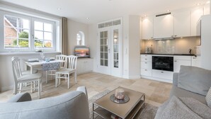 Eine moderne Küche mit weißen Schränken, ein Essbereich mit Tisch und Stühlen sowie ein Wohnzimmer mit Sofa und Couchtisch.