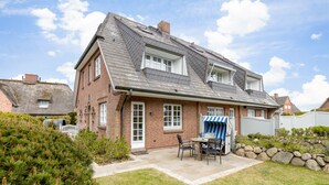 Ein zweistöckiges Haus mit Ziegelaußenwand, einer überdachten Terrasse mit Gartenmöbeln und einer Steinmauer zur Geländeerhöhung.