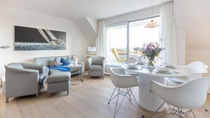 A modern living room with a dining area, featuring a large window with a view, a sofa set, and a dining table with chairs.
