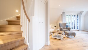 A spacious living area with a wooden staircase, a comfortable armchair, a coffee table, and a large window providing natural light.