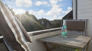 A small wooden table with a bottle of water on a balcony with a view of houses and trees. - 3-room apartment on the upper floor/ground floor with approx. 54 sqm floor space in Munkmarsch (Sylt)