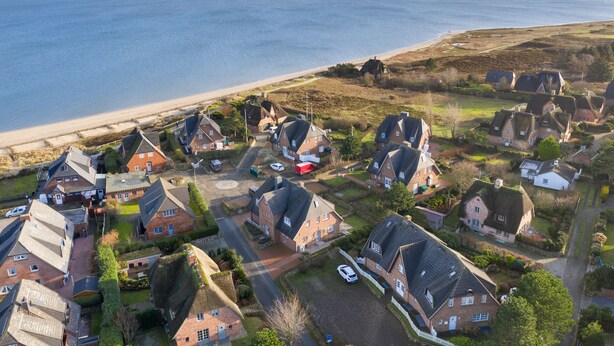 An aerial view of a coastal residential area with houses, a beach, and a clear sky. - 3-room apartment on the upper floor/ground floor with approx. 54 sqm floor space in Munkmarsch (Sylt)