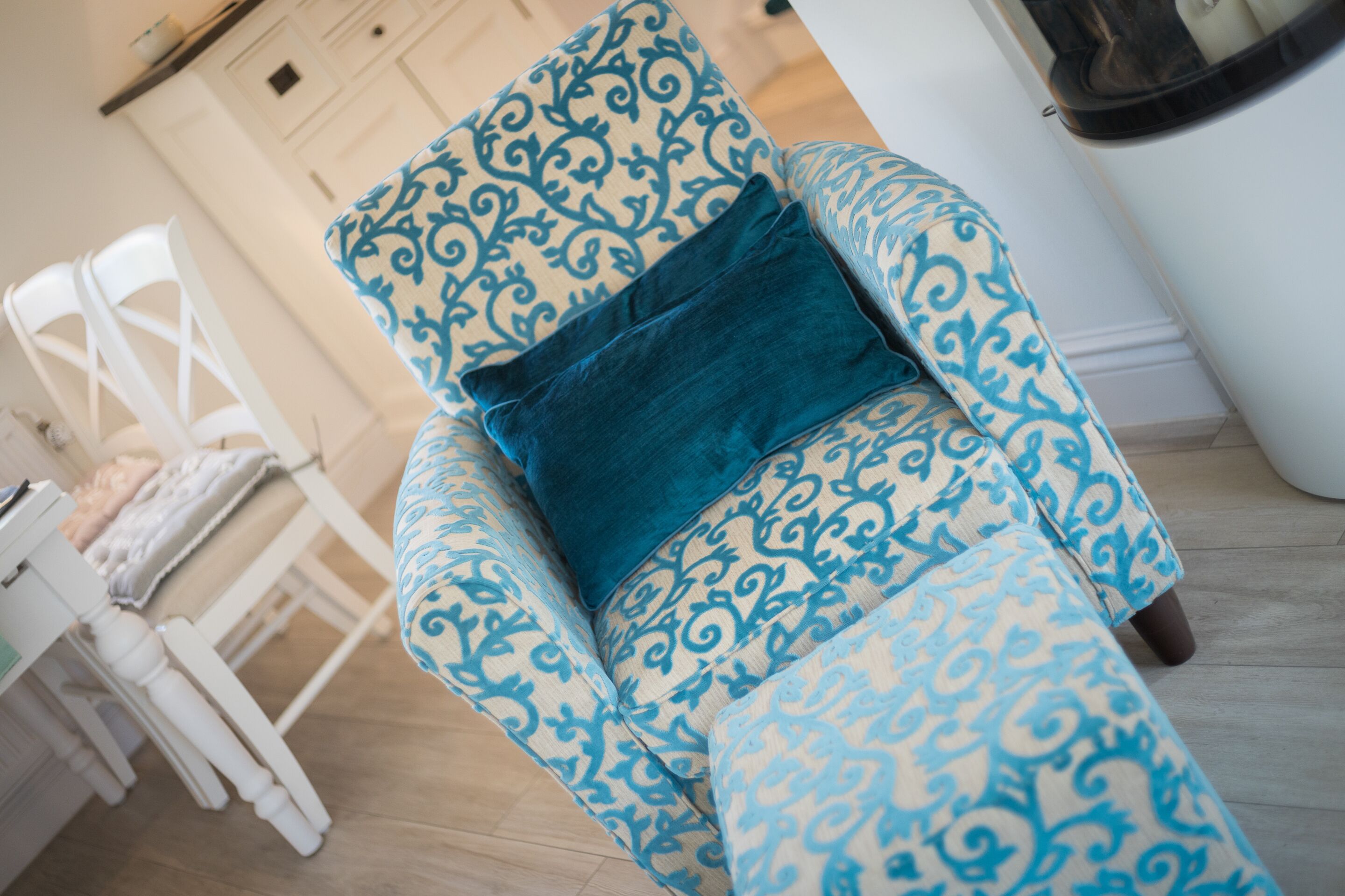 A patterned armchair with a blue cushion in a room with wooden flooring and white furniture.