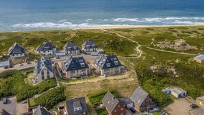 An aerial view of a coastal residential area with houses, a beach, and a clear sky.