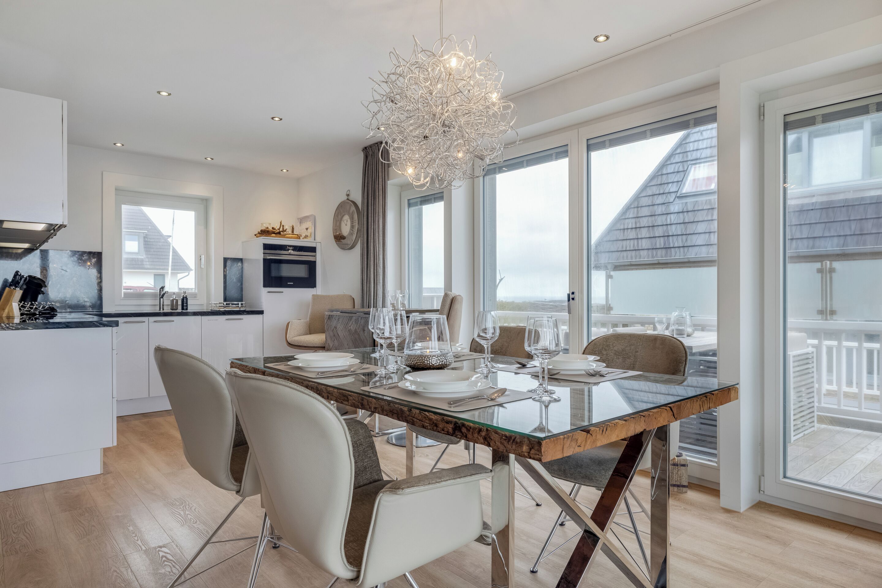 A modern kitchen with white cabinets, a built-in oven, and a dining area with a glass table and chairs.