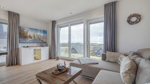 A modern living room with a large window, a sofa, a coffee table, and a flat-screen TV.