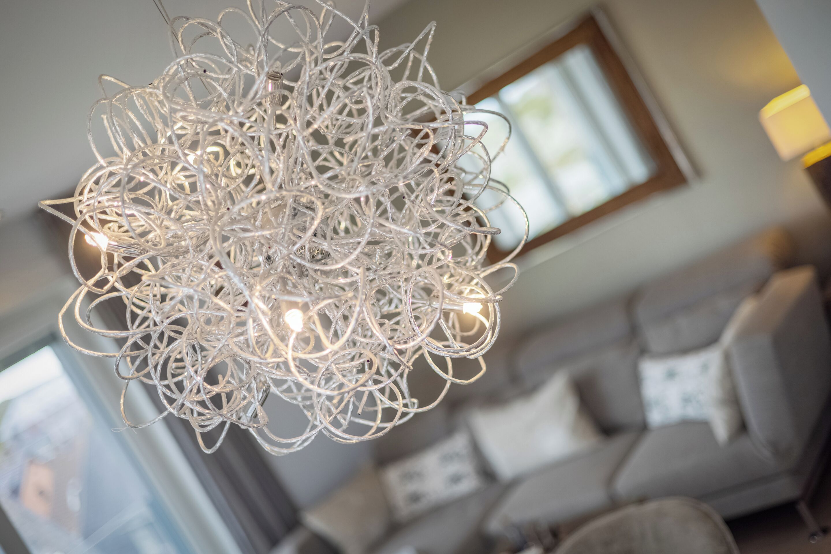 Ein Kronleuchter mit mehreren Lampen in einem Wohnzimmer mit Sofa und Fenster.