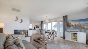 A modern living room with a sofa, a dining area, and a kitchen in the background.