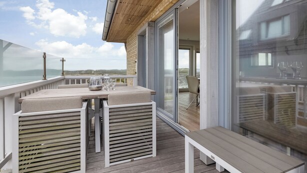 A deck with a table and benches, overlooking a body of water and a building.
