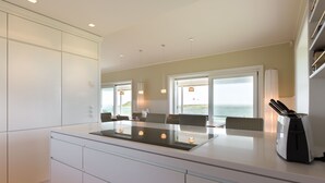 Una cocina moderna con una isla central, armarios blancos y vistas al océano a través de amplios ventanales.