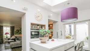 Eine moderne Küche mit Kochinsel, ein Essbereich mit Tisch und Stühlen, ein Wohnzimmer mit Sofa und ein großes Fenster mit Vorhängen.