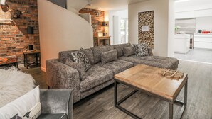 Ein modernes Wohnzimmer mit einem Ecksofa, einem Couchtisch aus Holz und einer Wand aus Ziegelsteinen.