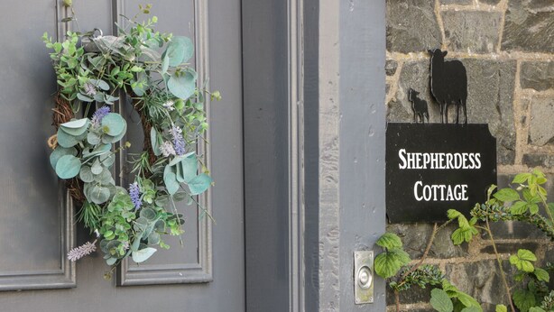 Eine graue Tür mit einem Kranz und einem Schild, auf dem 'Shepherdess Cottage' steht.
