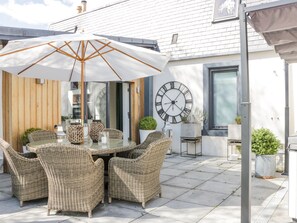 Eine Terrasse mit Korbmöbeln, einem großen Sonnenschirm und einer Wanduhr.