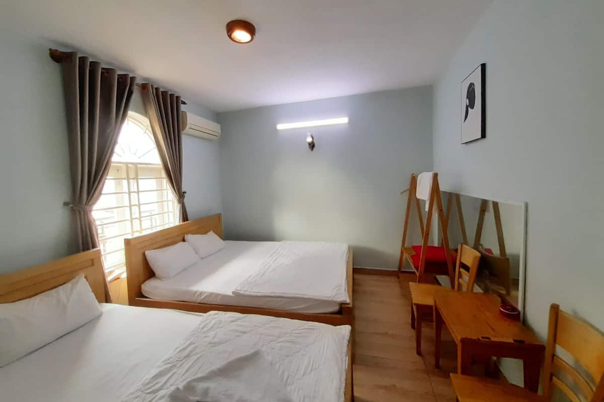 A hotel room with two beds, a desk, a chair, an easel, and a window with curtains.