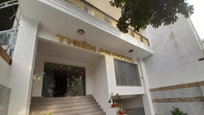 A hotel entrance with a staircase leading up to the door, potted plants, and a balcony with a railing. - Capital O 1221 Thien An Hotel (Ho Chi Minh City)
