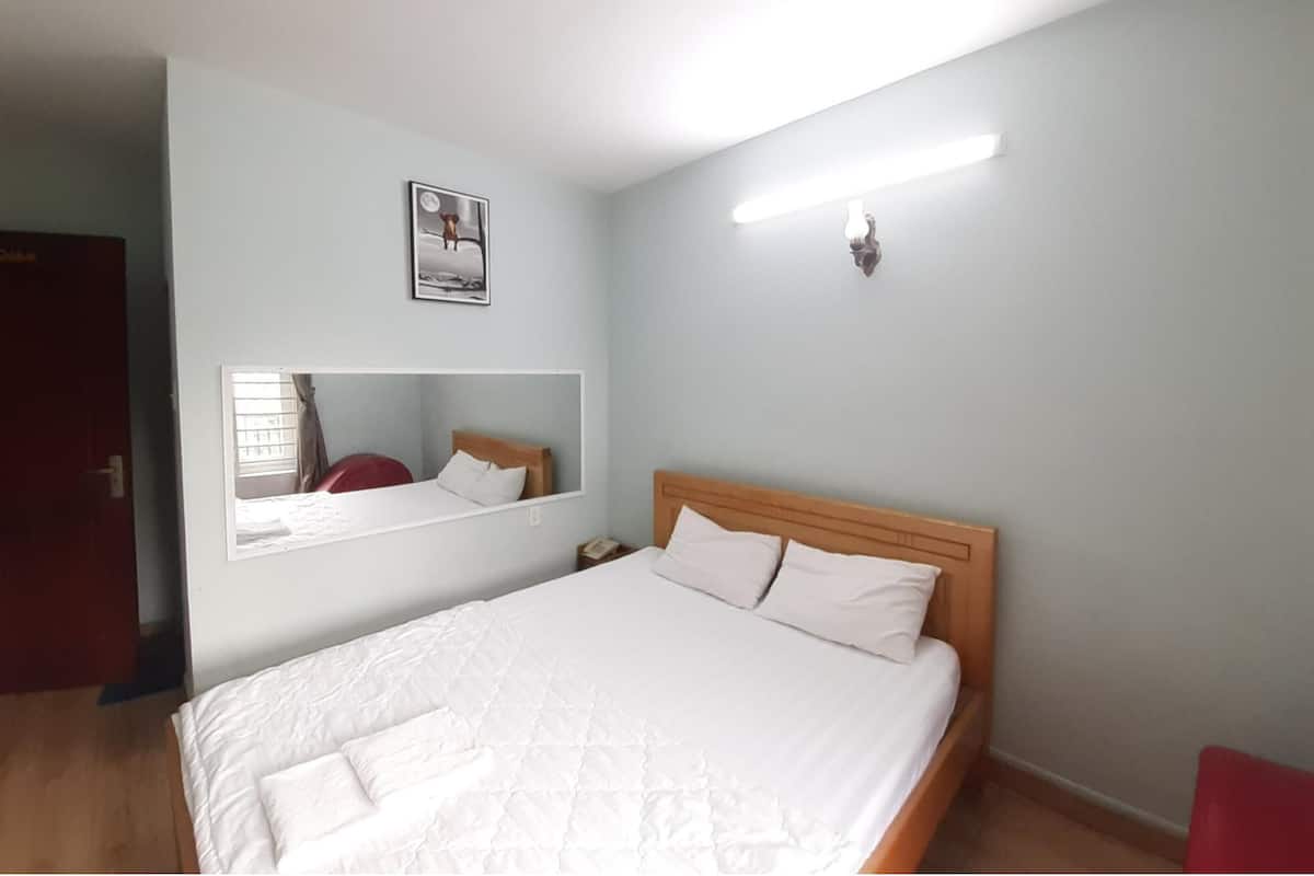 A bedroom with a bed, a nightstand, a wall-mounted mirror, and a light fixture.