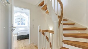 A modern staircase with wooden steps and white railings, leading to a bedroom with a bed and a window. - Hausteil mit ca. 95qm Nutzfläche im EG, UG, OG und DG (Hörnum (Sylt))