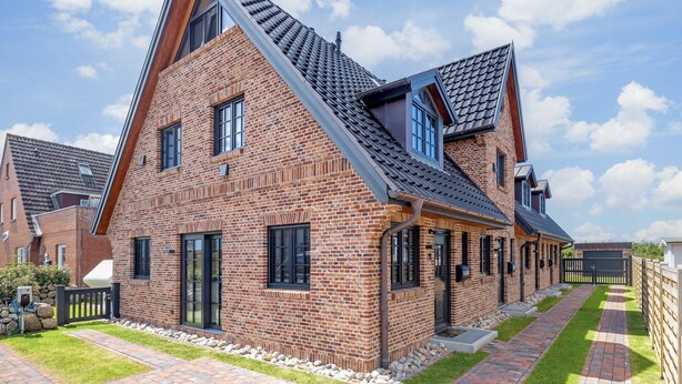 A modern two-story house with a sloped roof, brick exterior, and a paved driveway. - Hausteil mit ca. 95qm Nutzfläche im EG, UG, OG und DG (Hörnum (Sylt))