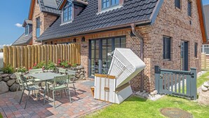 A brick house with a patio, a table with chairs, and a white folding chair. - Hausteil mit ca. 95qm Nutzfläche im EG, UG, OG und DG (Hörnum (Sylt))