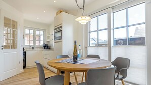 A modern kitchen with white cabinets, a built-in oven, and a dining area with a round wooden table and four chairs. - Hausteil mit ca. 95qm Nutzfläche im EG, UG, OG und DG (Hörnum (Sylt))