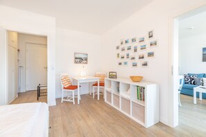 Quarto claro e moderno com piso de madeira, mobiliário branco, uma estante e uma parede decorada com pequenas imagens.
