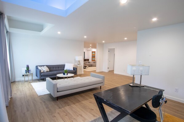 Un salon moderne avec un canapé, une table basse et une table à manger. Une lampe se trouve sur la table à manger. La pièce est dotée d’un plancher en bois et de murs blancs.