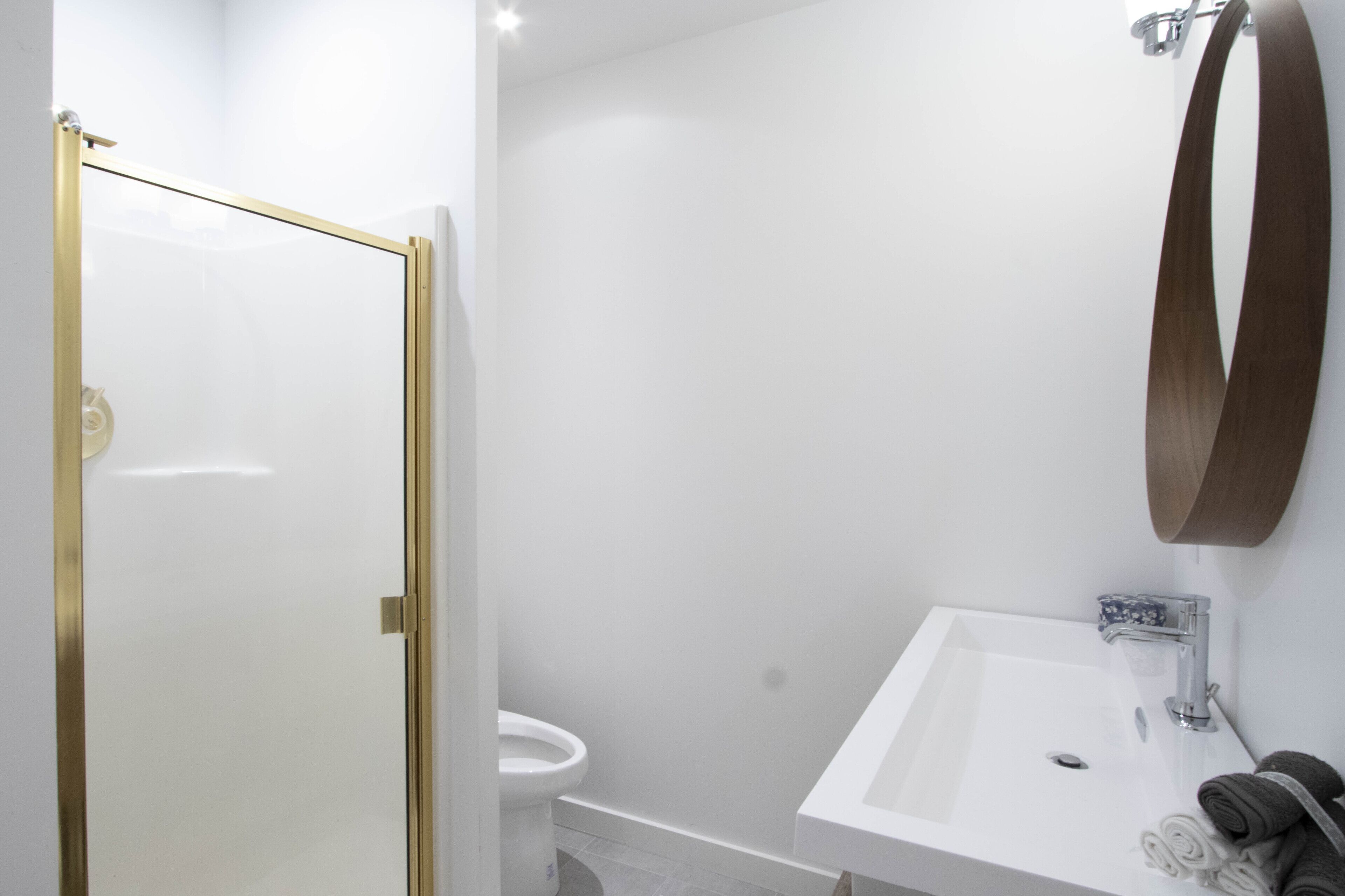 A bathroom with a glass shower door, a white sink, and a wooden-framed mirror.