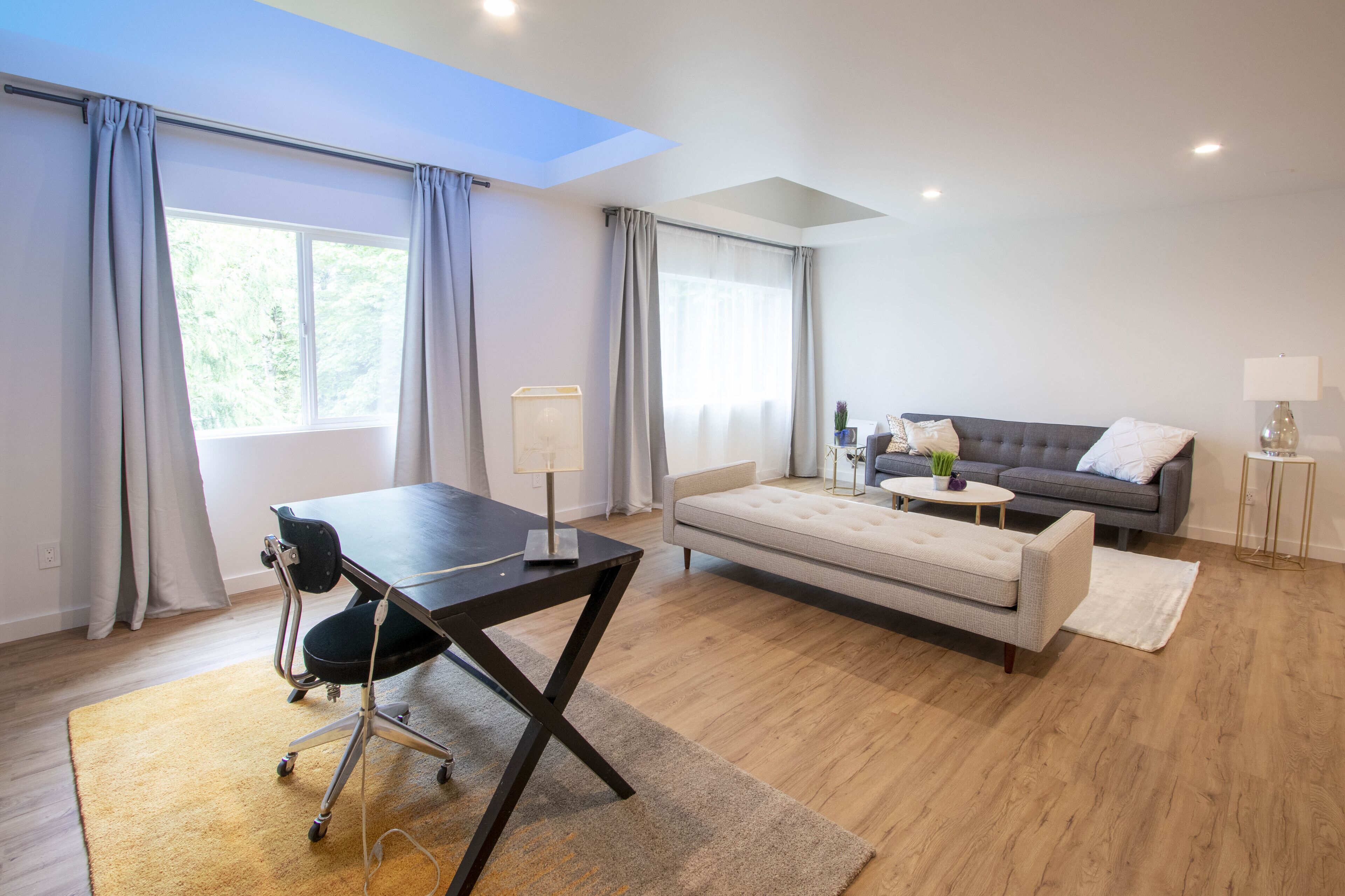 A modern living room with a dark wooden desk, a grey sofa, and a white rug.