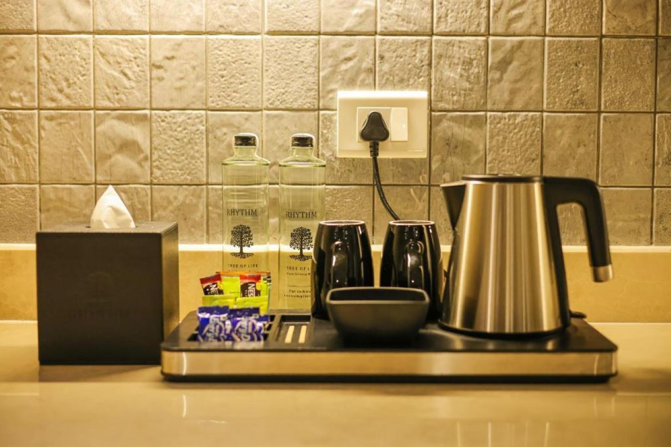 Una encimera de cocina con una cafetera, dos botellas, una caja de pañuelos y una bandeja.