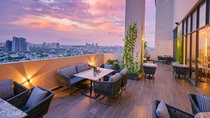 A rooftop terrace with outdoor seating, a city view, and a sunset sky. - Rhythm Gurugram, Hotel & Suites, Sohna Road - Sector 68 (Gurugram)
