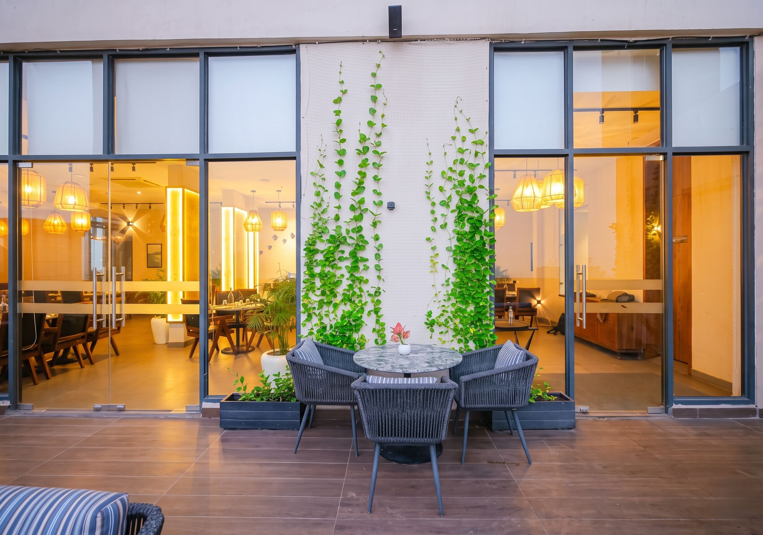 A modern outdoor seating area with a round table and chairs, surrounded by glass doors leading to an interior space.